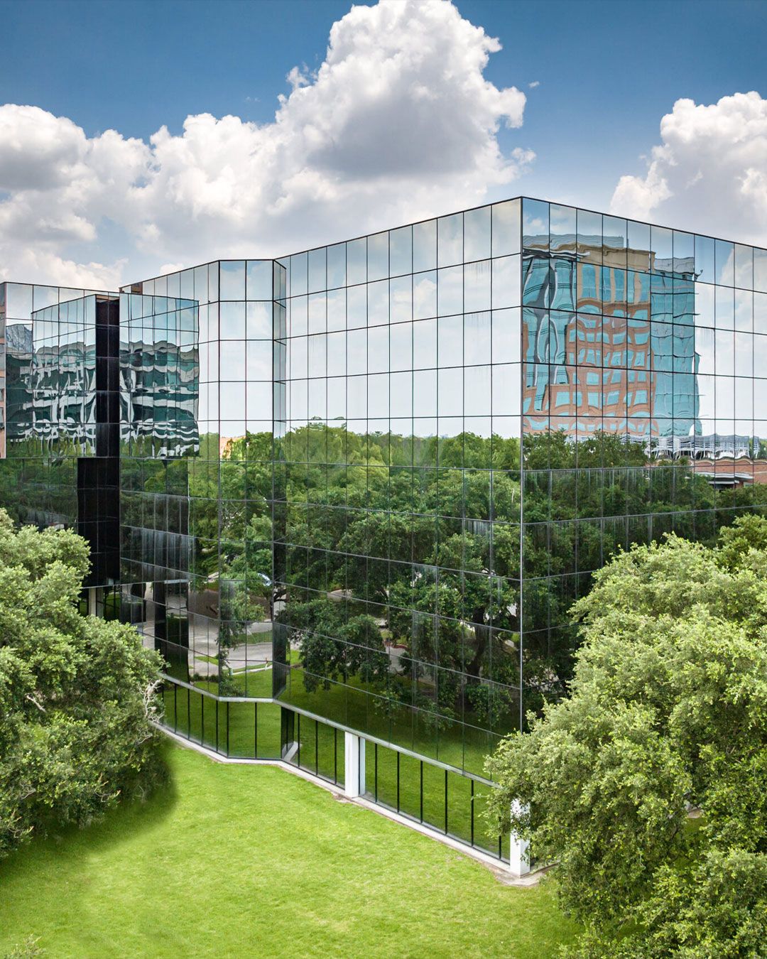 Modern glass office building reflecting blue sky and green landscape